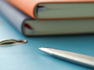 Silver pen lying at blue binder folder among set of notepads