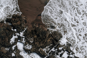 Fototapeta premium Top view aerial photo from flying drone of ocean landscape with big waves and rocks on black sand beach. Copy space for your advertising text message or promotional content.Perfect website background