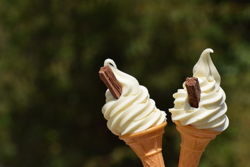 Two soft whipped ice cream cones with chocolate flakes against a blurred background with copy space