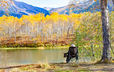 The woman in chair for camping, admiring the lake and mountains