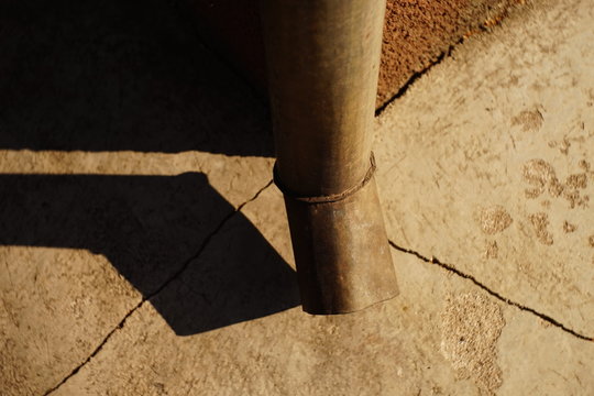 Downpipe at the corner of the building, cracks in the blind area of the house, sunlight and shadow from the drain pipe