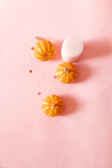 Halloween composition of pink candles, small pumpkins and glitter decor over pink background. Top view, place for text.