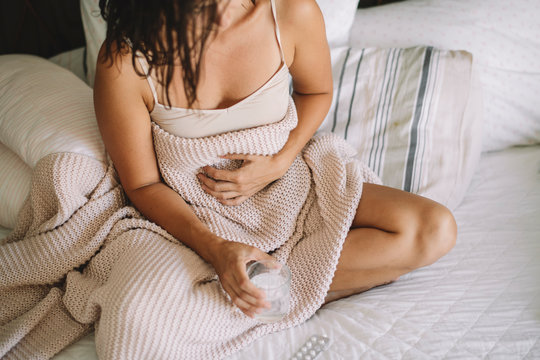 Young woman sick in bed holding glass of water