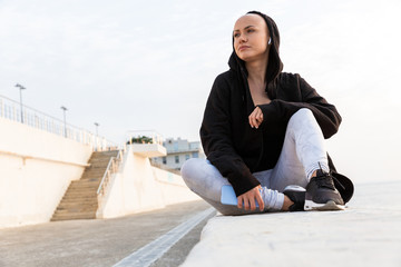 Image of young bald woman using cellphone and earphone while sitting