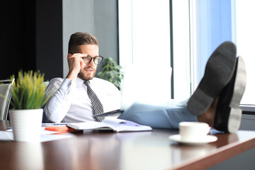 Handsome businessman sitting with legs on table and smiling in office