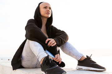 Image of focused bald woman using cellphone while sitting