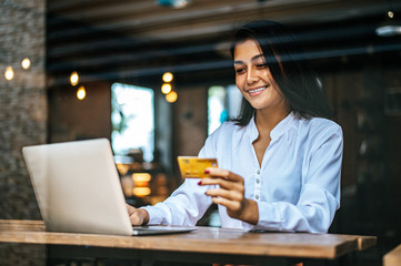 woman sat with a laptop and paid with a credit card in a coffee shop.