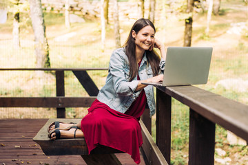 Happy smiling young brunette girl with laptop on a park background. Freelancer at work in the fresh air.