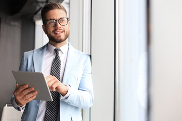 Fototapeta premium Modern business man in formalwear using digital tablet while standing near window in the office
