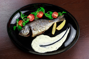 baked dorado with sauce, lemon, tomatoes and herbs in a plate