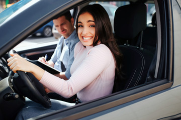 Male auto instructor takes exam in young woman. Confused stressed young woman drive car careless. Model look on camera. Unhappy young instructor sit besides.