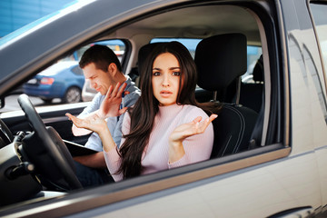 Male auto instructor takes exam in young woman. Confused stressed model look on camera. Instructor examining girl. Sit together in car.