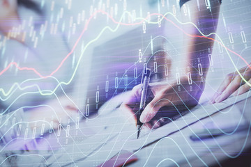 A woman hands writing information about stock market in notepad. Forex chart holograms in front. Concept of research. Double exposure