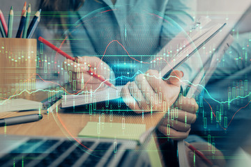 A woman hands writing information about stock market in notepad. Forex chart holograms in front. Concept of research. Multi exposure