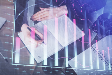 Forex chart hologram on hand taking notes background. Concept of analysis. Multi exposure