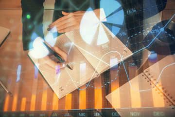 Forex chart hologram on hand taking notes background. Concept of analysis. Multi exposure