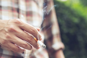 man holding smoking a cigarette in hand. Cigarette smoke spread in public areas outdoor. tobacco