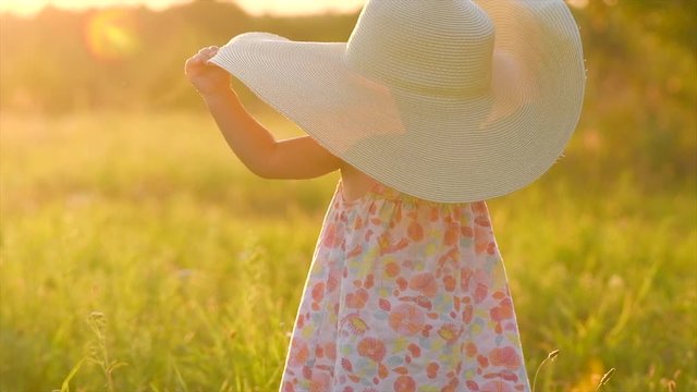 Adorable little baby girl on a field, enjoying nature outdoors wearing wide brimmed straw hat. Beautiful cute little funny one year old child smiling and doing her first steps. Slow motion 4K UHD