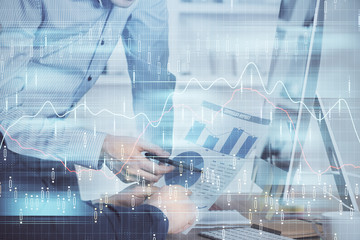 Double exposure of chart with businessman typing on computer in office on background. Concept of hard work.