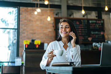 woman sitting happily working with a smartphone in a coffee shop and notebook.