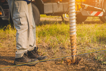 technician installing ground screw for mounting structure of solar panel at solar farm
