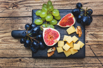 Cheese cubes, fresh fruit figs grapes Honey walnut on wooden chopping Board. Selective focus. Close up.