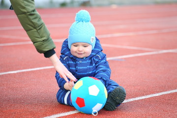 baby sits in a sports stadium. with color ball