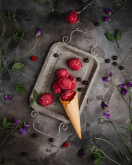 berry ice cream scoops in single waffle cone on vintage metal tray with fresh berries and flowers,...