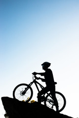 Fototapeta na wymiar Silhouette of the athlete standing on the rock with bicycle