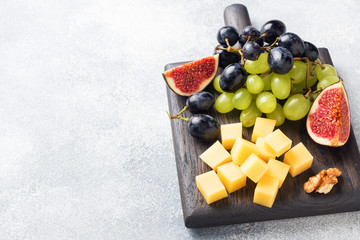 Cheese cubes, fresh fruit figs grapes Honey walnut on wooden chopping Board. Copy space.