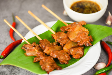 Grilled pork thai asian street food style - Slice pork skewer sticks grilled on banana leaf on white plate with sauce chilli garlic