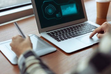 Close up on a man's hands while using a pen tablet to create a graphic design on his laptop computer. Communicate about remote creative work and using a digital stylus to draw inside his program