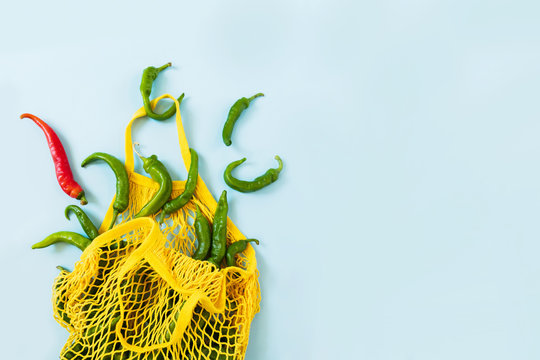 Creative layout green chilli peppers. Green vegetables in yellow string bag on pastel blue background. Heap of green hot pepper called frigitelli