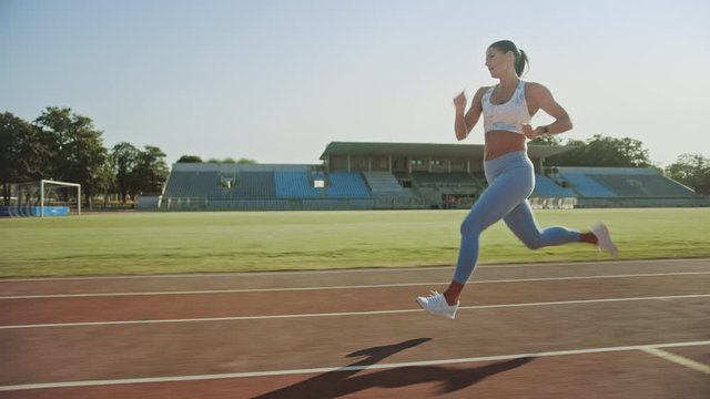 Beautiful Fitness Woman in Light Blue Athletic Top and Leggings Jogging in a Stadium. She is Running on a Warm Summer Afternoon. Athlete Doing Her Routine Sports Practice on a Track. Slow Motion.