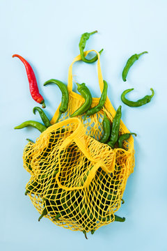 Creative layout green chilli peppers. Green vegetables in yellow string bag on pastel blue background. Heap of green hot pepper called frigitelli