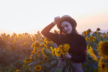 Beautiful lovely girl in a straw hat enjoying nature on a field of sunflowers. Sunset. Autumn time