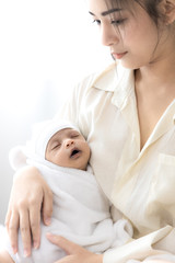 Mother carrying her baby in white bed room. Cute newborn baby sleeping in mother 's arm. Housewife and mother 's day concept.