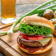 Delicious cheeseburger with baked potatoes, broccoli and scallion on a cutting board served with a glass of lager beer. Close-up shot.