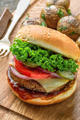 Classic hamburger with tomato, lettuce and onion served with grilled potatoes and broccoli on a wooden table.
