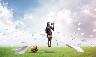 Woman with megaphone sitting on big light bulb