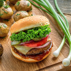 Delicious cheeseburger with baked potatoes, broccoli and scallion on a cutting board served with a glass of beer. Close-up shot.