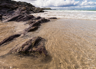Incoming tide on the beach at Hayle Bay, Cornwall, England UK on a sunny day with rocks and waves.