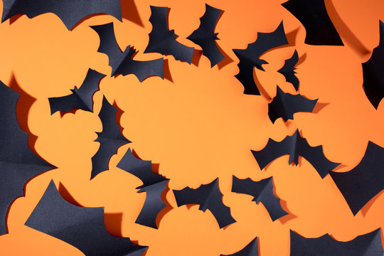 Photo of black bats on blank orange background, flying in circle.