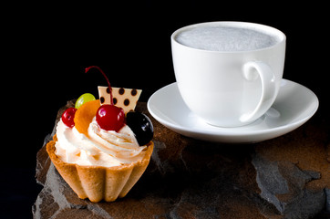 Fruit cake with cherries, grapes and plum stands on a wild stone next to a white cup of coffee with a foam