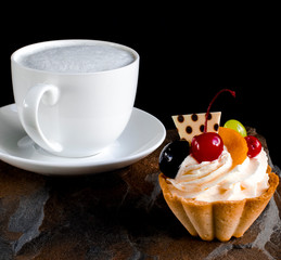 Fruit cake with cherries, grapes and plum stands on a wild stone next to a white cup of coffee with a foam