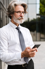 Photo of serous mature businessman typing on cellphone