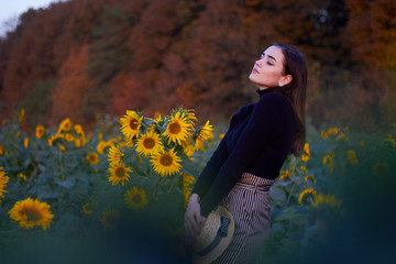 Beautiful lovely girl with a straw hat enjoying nature on a field of sunflowers. Sunset. Autumn time