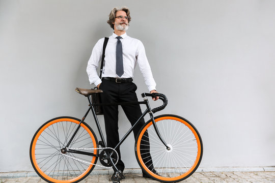 Photo of modern elderly businessman standing with bicycle