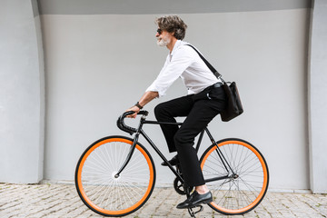 Photo of modern old businessman riding bicycle over gray wall