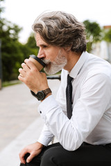 Photo of focused bearded businessman drinking coffee takeaway